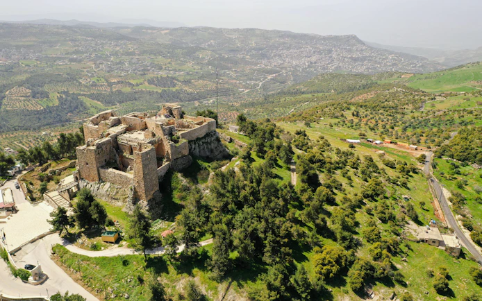 Ajloun Castle in northern Jordan surrounded by lush green hills and distant mountains.