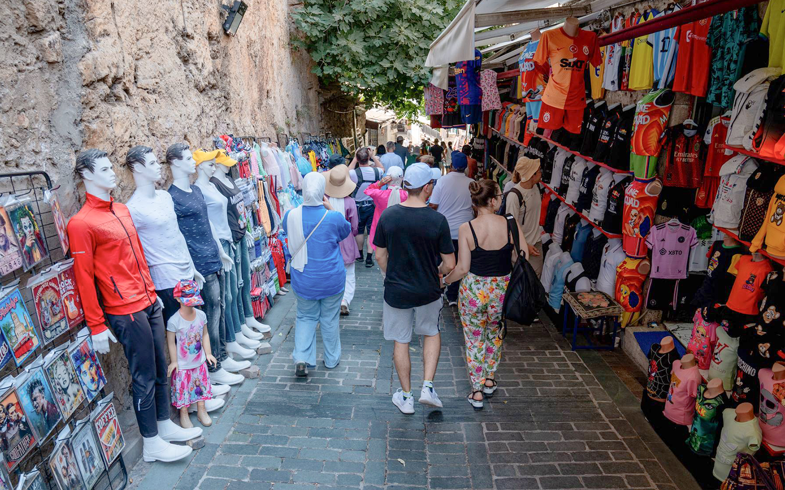 Street market in Antalya with tourists browsing clothing and souvenirs.