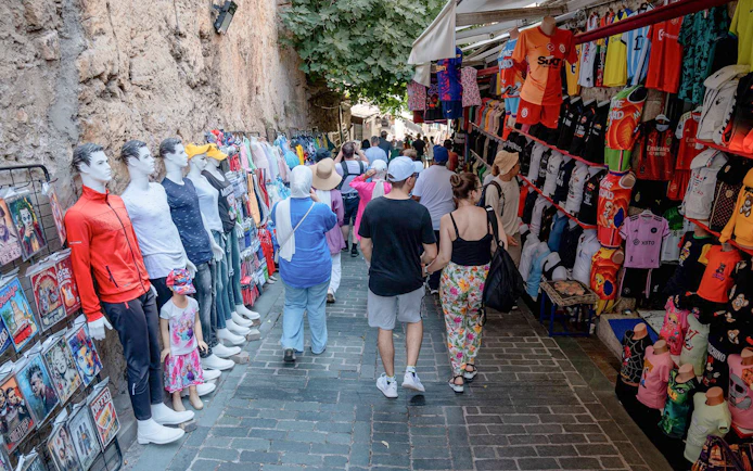 Street market in Antalya with tourists browsing clothing and souvenirs.
