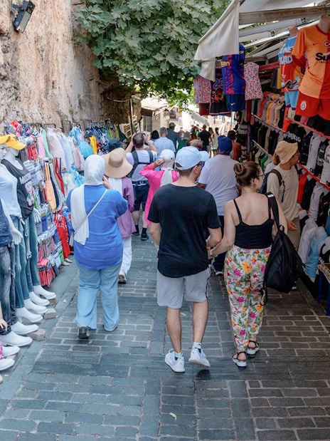 Street market in Antalya with tourists browsing clothing and souvenirs.