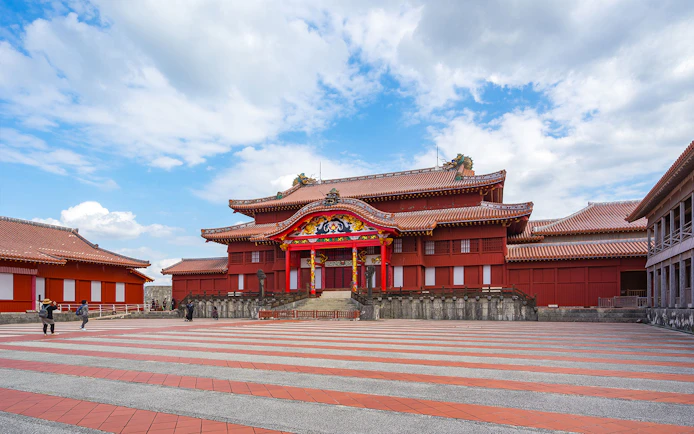 Shuri Castle in Okinawa, Japan, with traditional red architecture and tourists exploring the site.