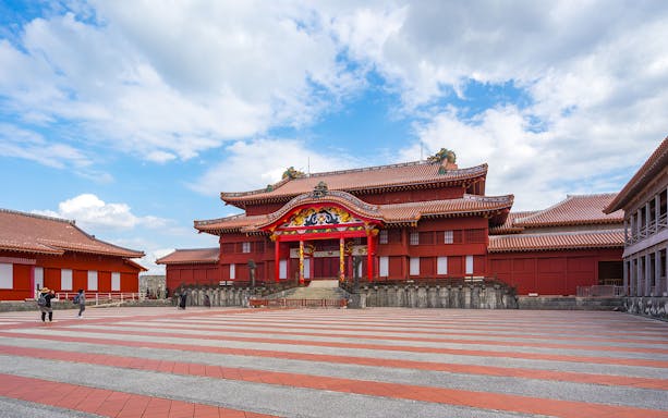 Shuri Castle in Okinawa, Japan, with traditional red architecture and tourists exploring the site.