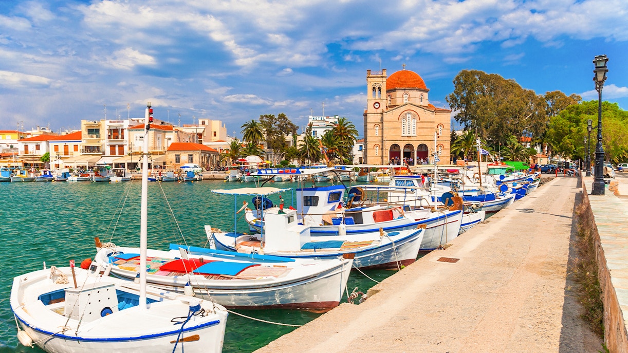 Boats docked at Aegina Island harbor with a church and buildings in the background, Greece.