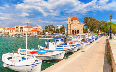 Boats docked at Aegina Island harbor with a church and buildings in the background, Greece.