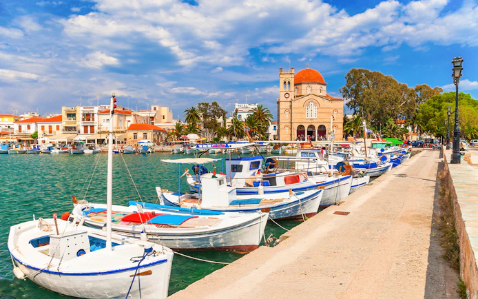 Boats docked at Aegina Island harbor with a church and buildings in the background, Greece.