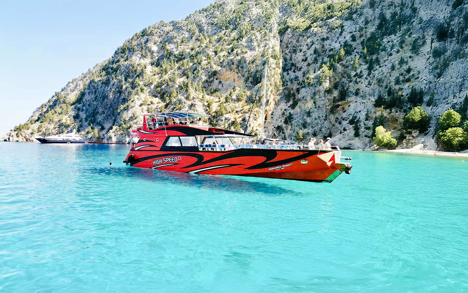 High-speed cruise boat on turquoise waters near rocky cliffs in Rhodes.