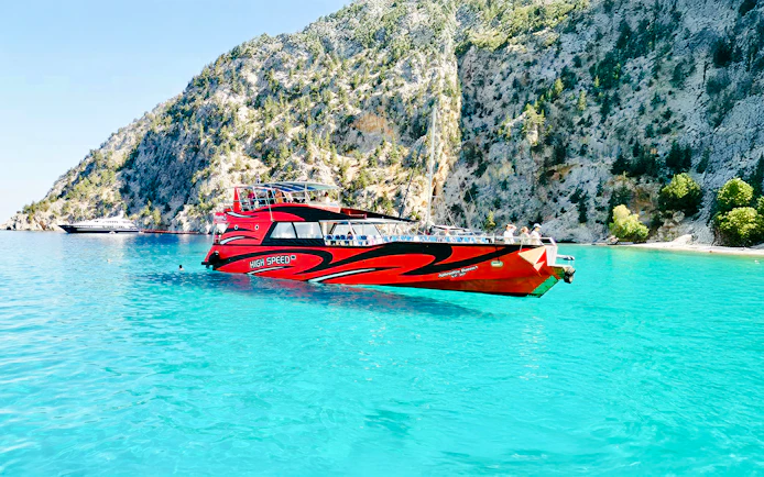 High-speed cruise boat on turquoise waters near rocky cliffs in Rhodes.