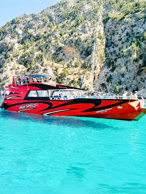 High-speed cruise boat on turquoise waters near rocky cliffs in Rhodes.