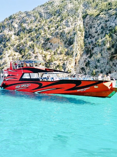 High-speed cruise boat on turquoise waters near rocky cliffs in Rhodes.