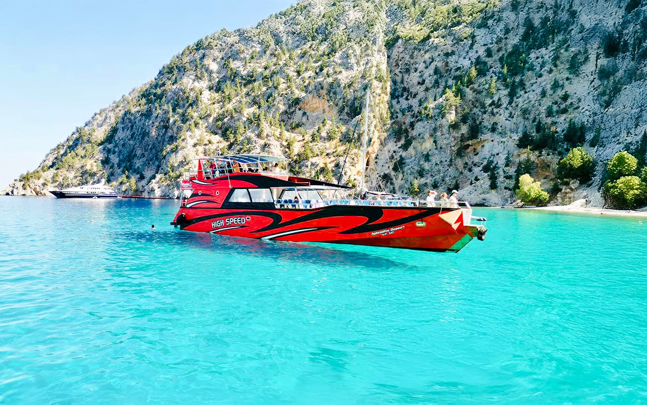 High-speed cruise boat on turquoise waters near rocky cliffs in Rhodes.
