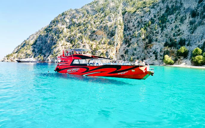 High-speed cruise boat on turquoise waters near rocky cliffs in Rhodes.