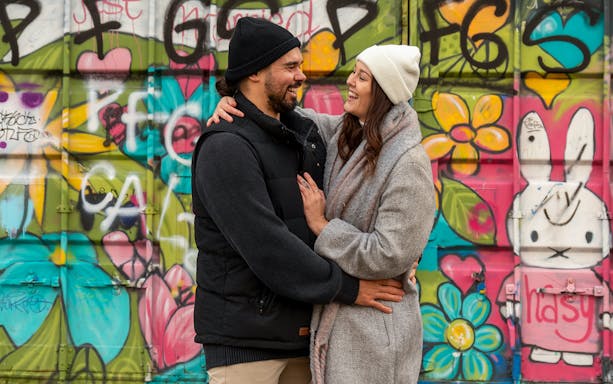 Couple smiling in front of colorful graffiti at NDSM, Amsterdam.