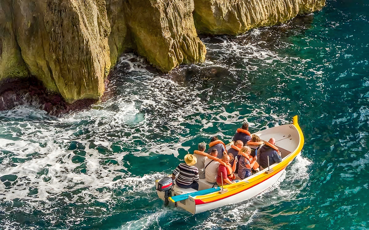 Boat tour near limestone cliffs at Blue Grotto, Malta.