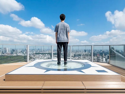 Person standing on Shibuya Sky observation deck overlooking Tokyo cityscape.