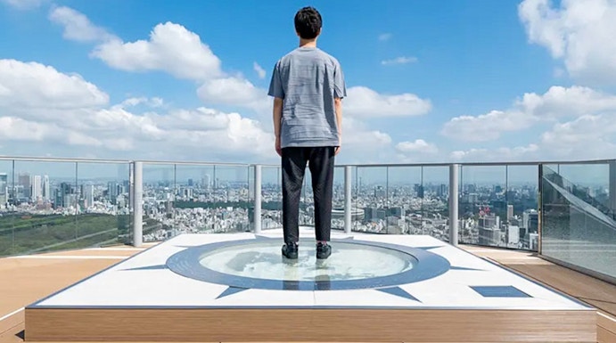 Person standing on Shibuya Sky observation deck overlooking Tokyo cityscape.