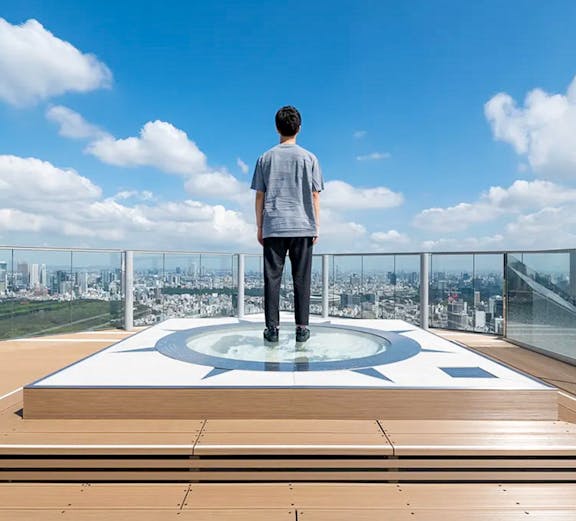 Person standing on Shibuya Sky observation deck overlooking Tokyo cityscape.