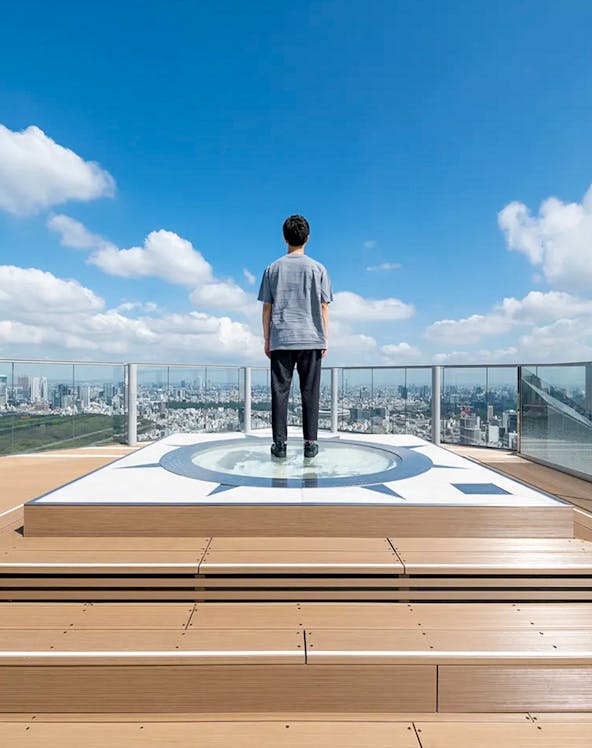 Person standing on Shibuya Sky observation deck overlooking Tokyo cityscape.