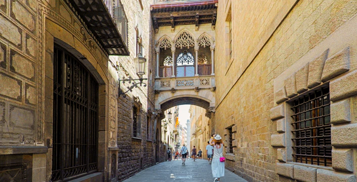 Narrow street in El Raval District, Barcelona, with historic architecture and tourists walking.