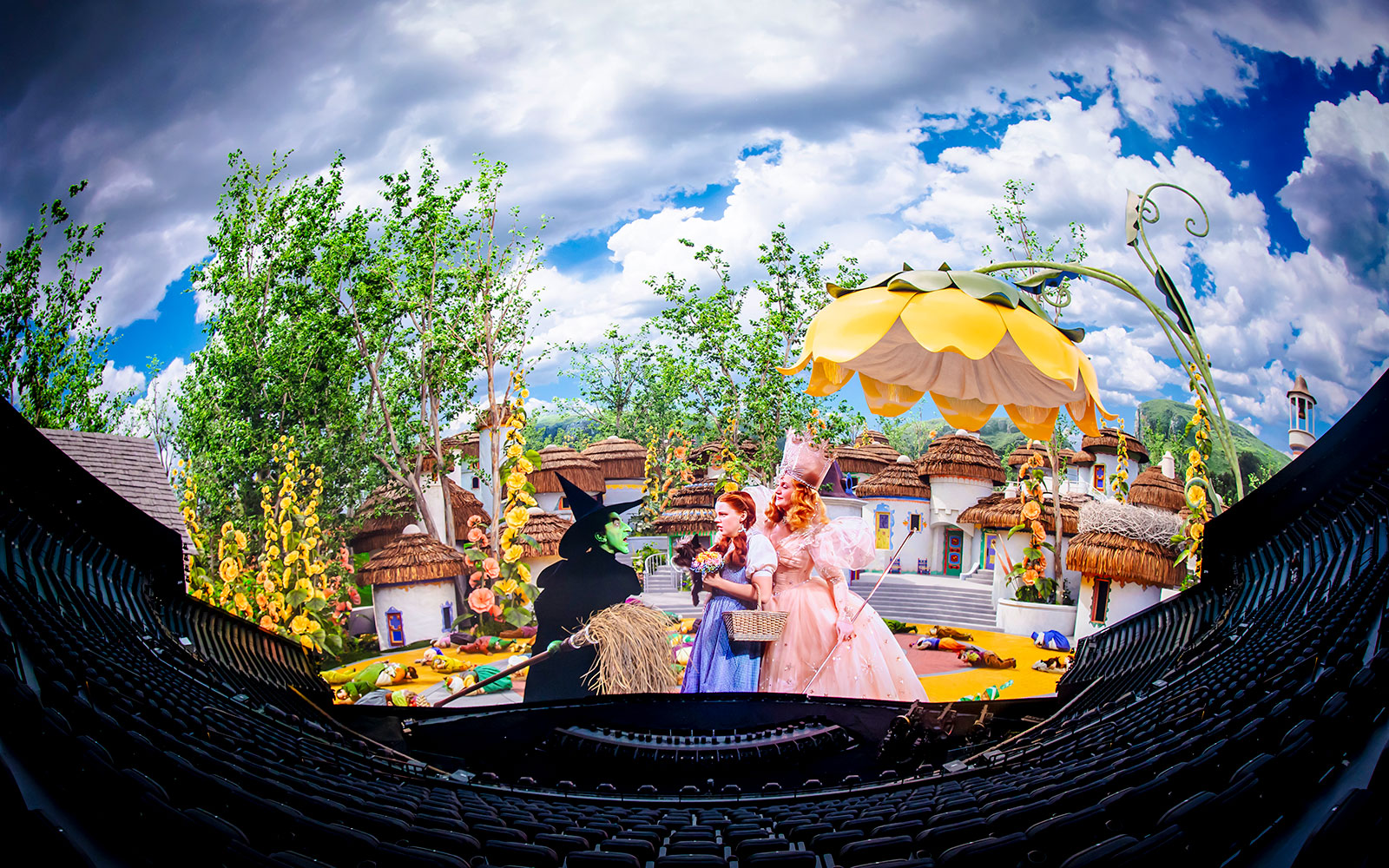 Scene from Wizard of Oz show at Sphere with characters in colorful village setting.