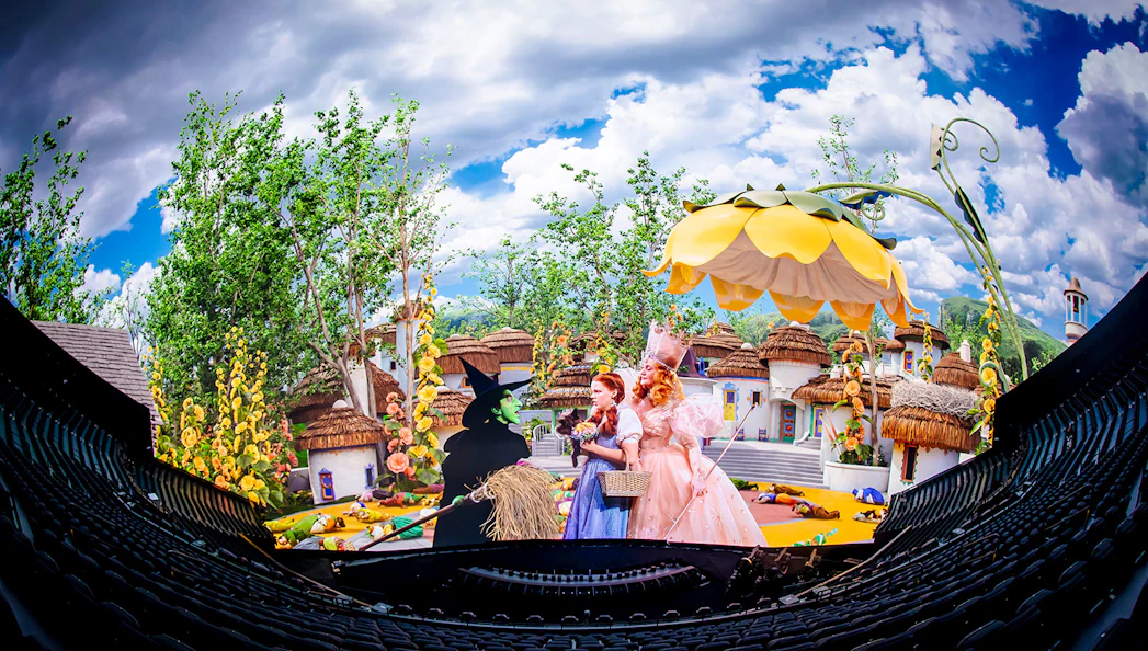 Scene from Wizard of Oz show at Sphere with characters in colorful village setting.
