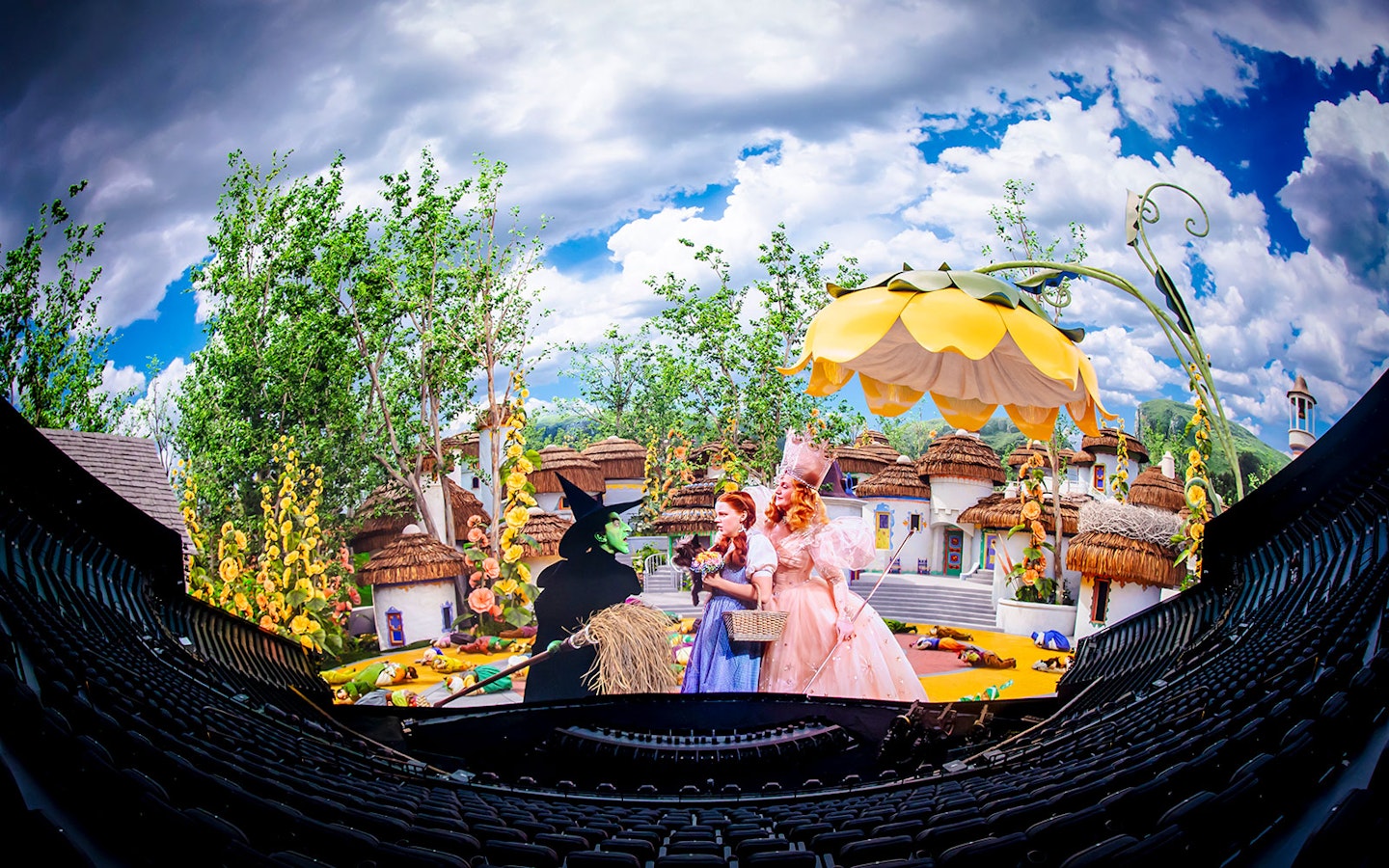Scene from Wizard of Oz show at Sphere with characters in colorful village setting.