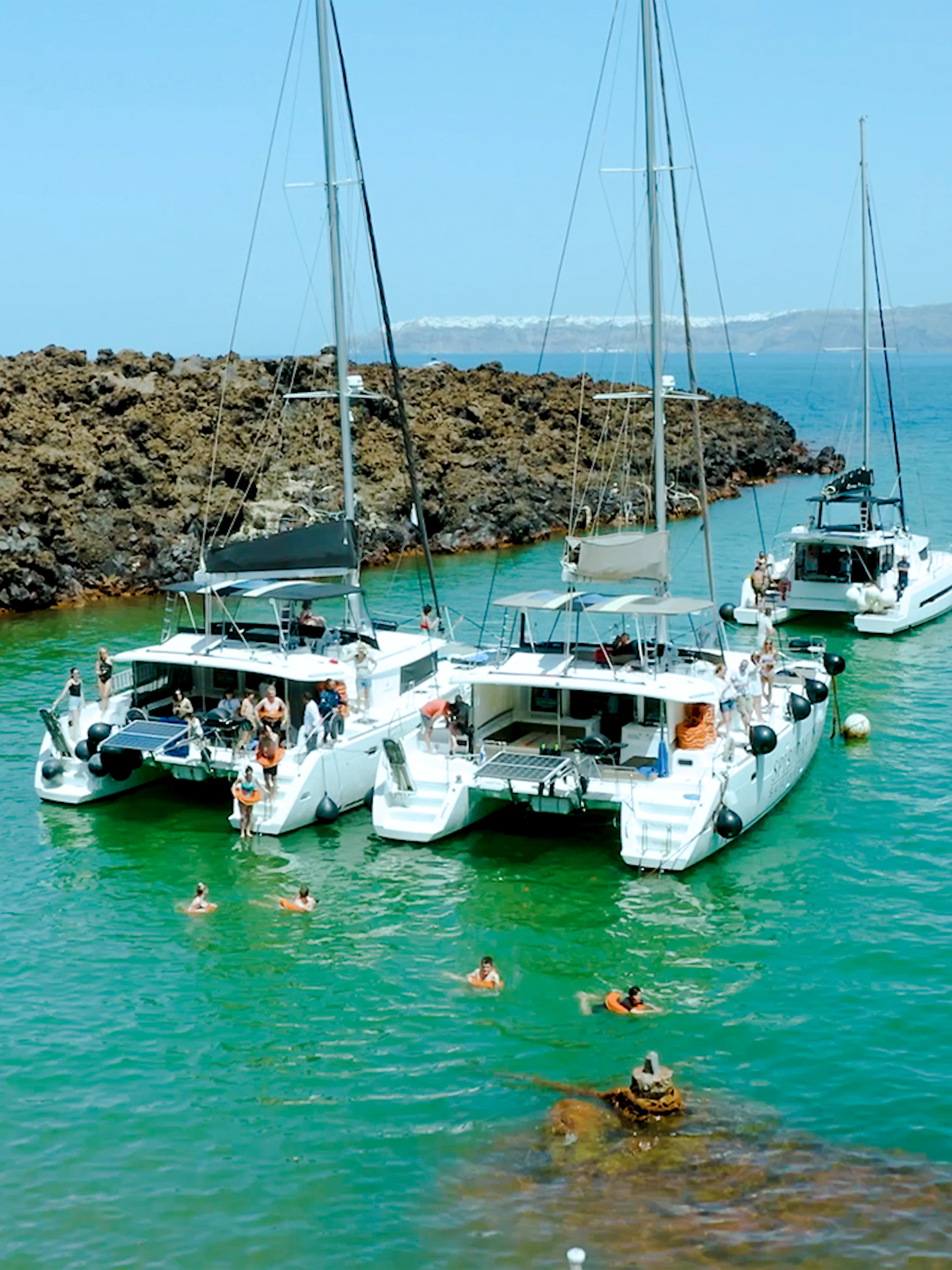 Catamarans anchored near volcanic rocks on Santorini Joy Daytime Cruise.