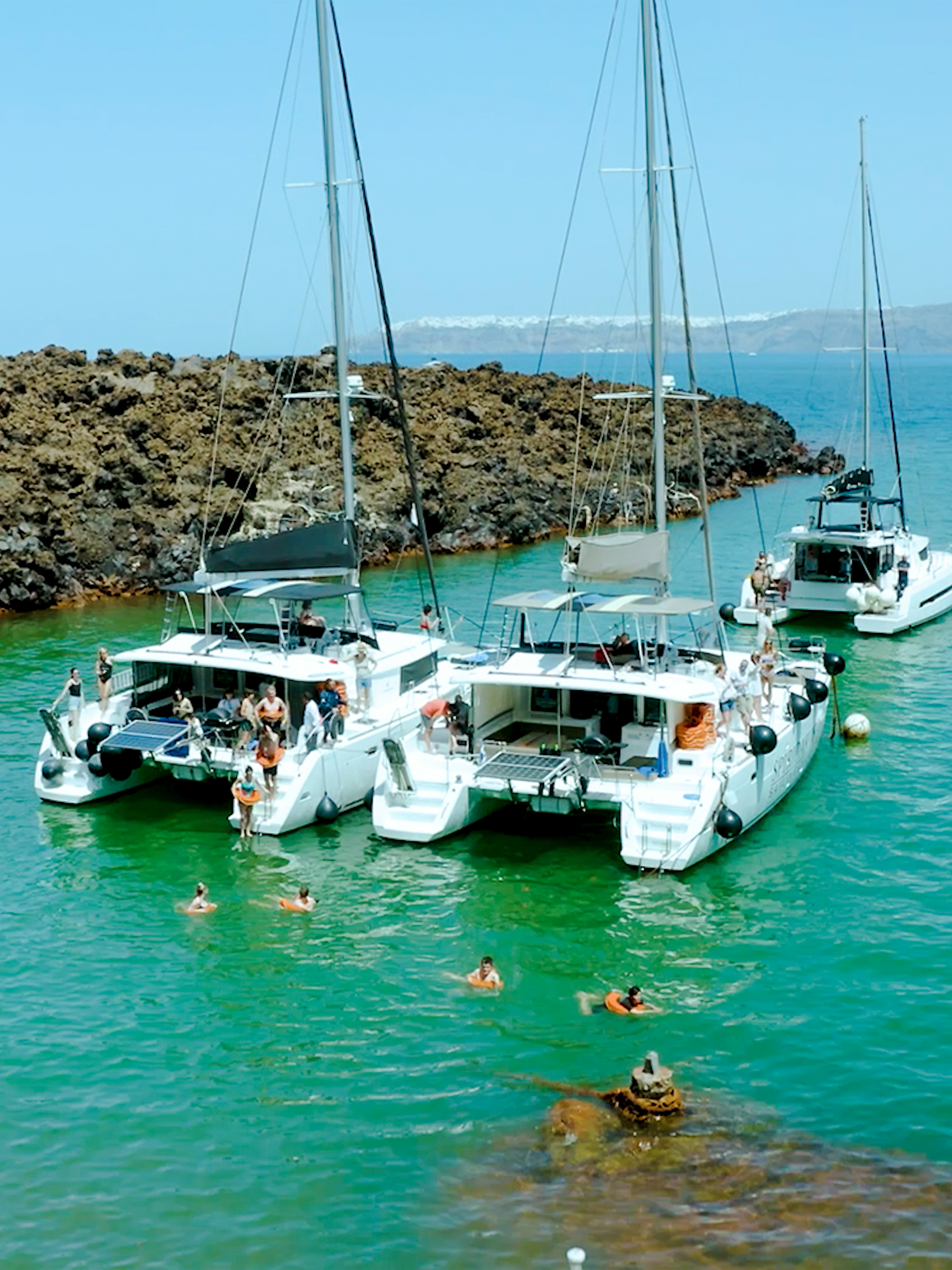 Catamarans anchored near volcanic rocks on Santorini Joy Daytime Cruise.