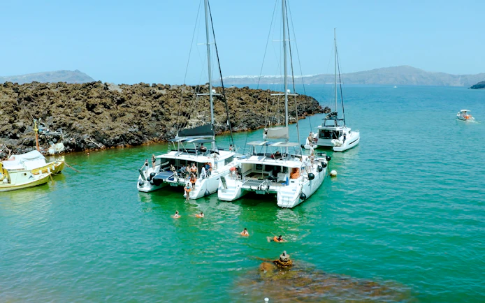 Catamarans anchored near volcanic rocks on Santorini Joy Daytime Cruise.
