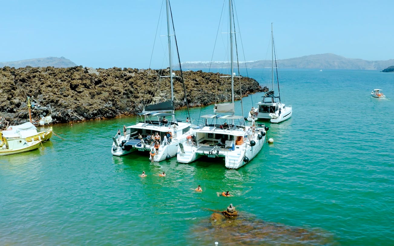 Catamarans anchored near volcanic rocks on Santorini Joy Daytime Cruise.
