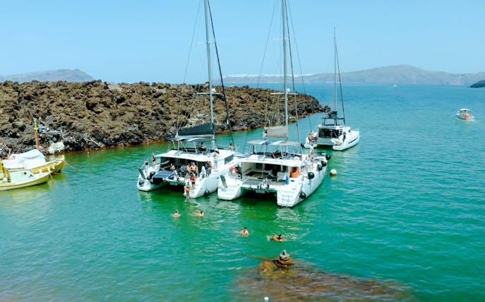 Catamarans anchored near volcanic rocks on Santorini Joy Daytime Cruise.