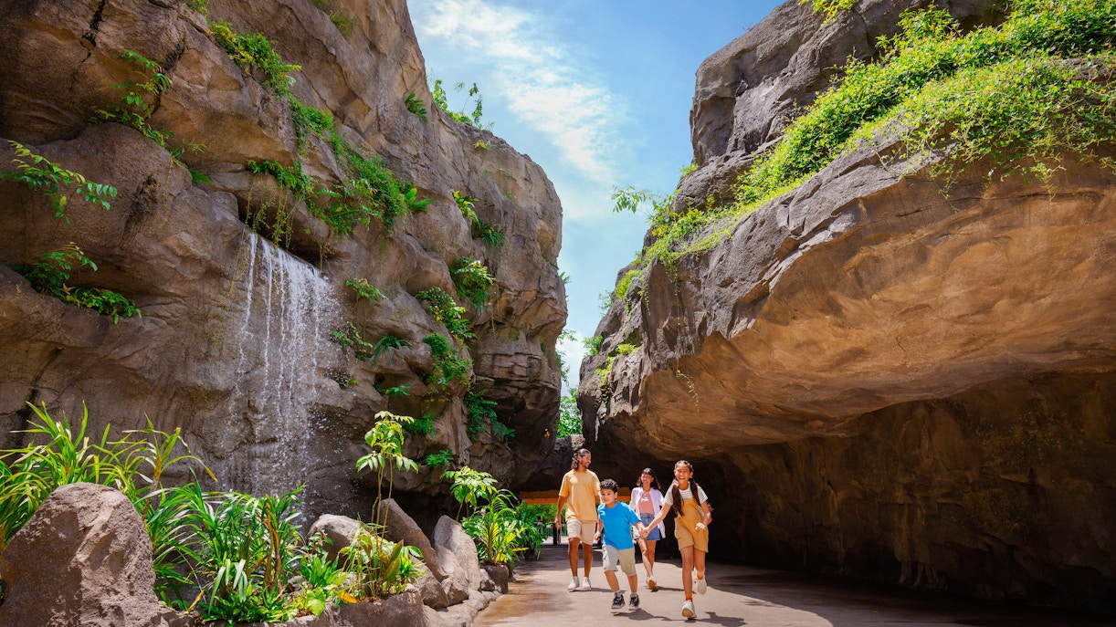 Family walking through lush Entrance Gorge with waterfall and rocky cliffs.