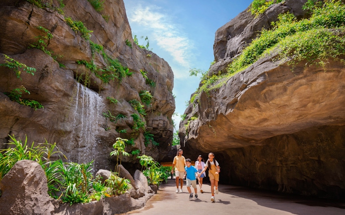 Family walking through lush Entrance Gorge with waterfall and rocky cliffs.