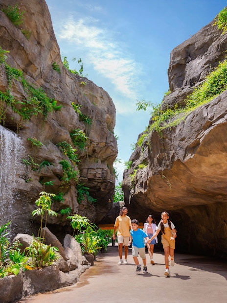 Family walking through lush Entrance Gorge with waterfall and rocky cliffs.