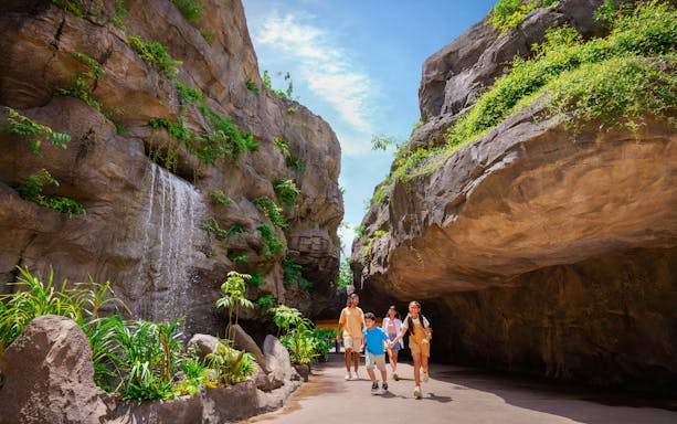 Family walking through lush Entrance Gorge with waterfall and rocky cliffs.