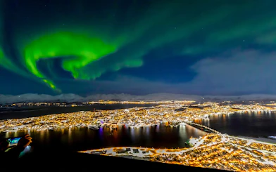 Northern lights over Tromso, Norway, with city lights reflecting on the water.