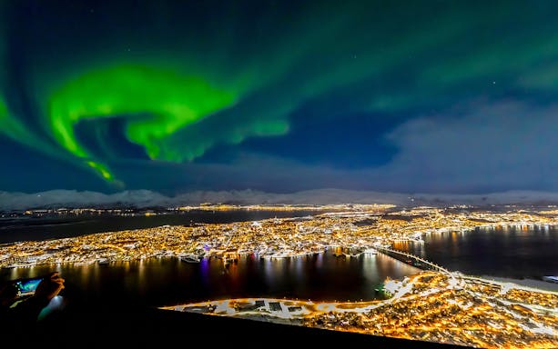 Northern lights over Tromso, Norway, with city lights reflecting on the water.