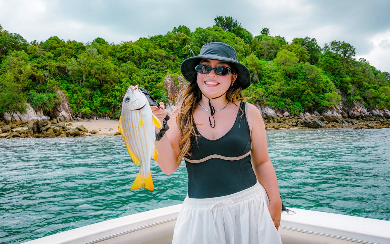 Woman holding fish on yacht near tropical shoreline.