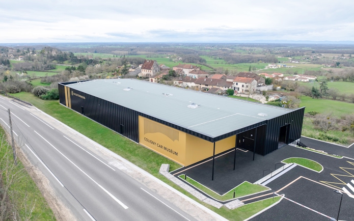 Coligny Car Museum building in Lyon, France, surrounded by countryside and village houses.