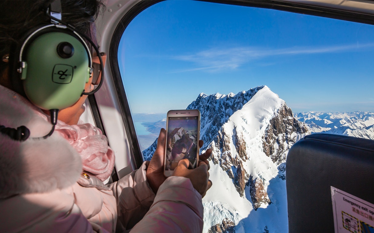 Lady photographing Mt Cook from helicopter during scenic flight tour.