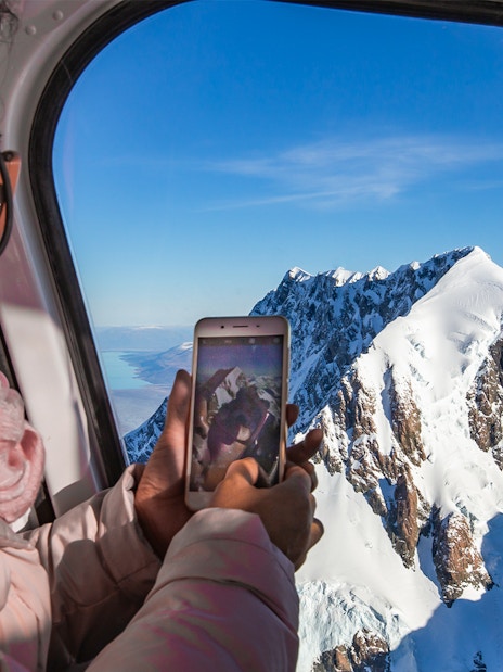 Lady photographing Mt Cook from helicopter during scenic flight tour.