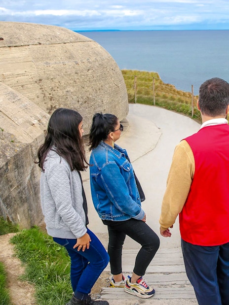 Tourists exploring Pointe du Hoc cliffs in Normandy with ocean view.