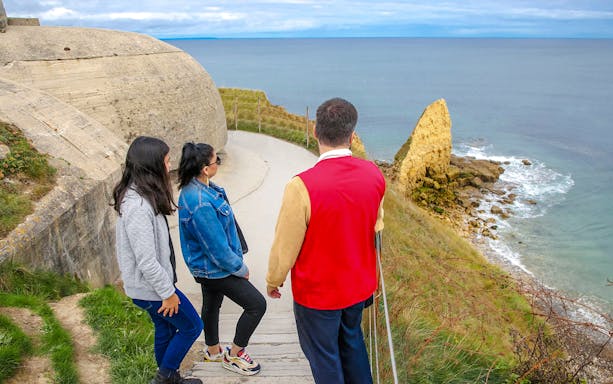 Tourists exploring Pointe du Hoc cliffs in Normandy with ocean view.