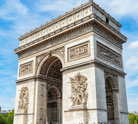 Arc de Triomphe in Paris with detailed sculptures and tourists nearby.