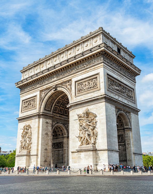 Arc de Triomphe in Paris with detailed sculptures and tourists nearby.