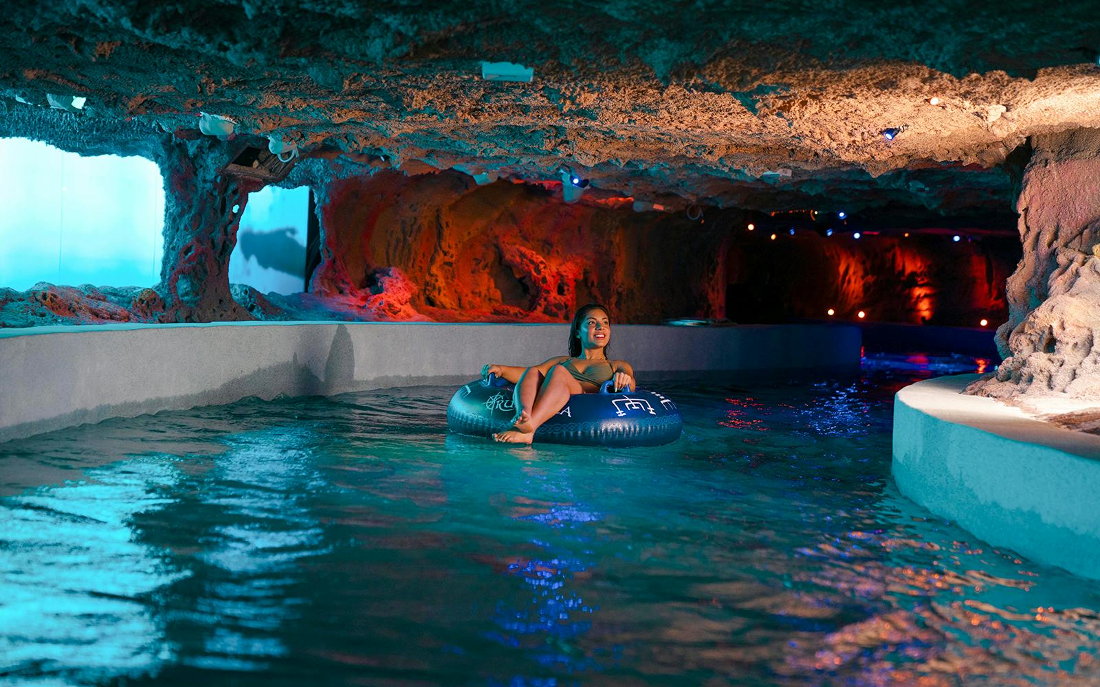 Person floating on a tube in the lazy river at Rulantica water park cave.