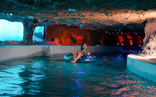 Person floating on a tube in the lazy river at Rulantica water park cave.