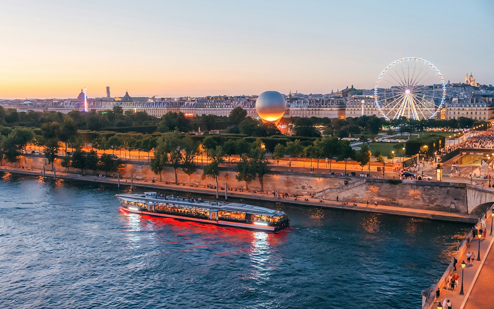 Seine River cruise boat passing by Paris landmarks at sunset with Ferris wheel in view.