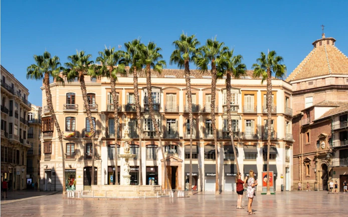 Plaza de la Constitución in Malaga with palm trees and historic buildings.