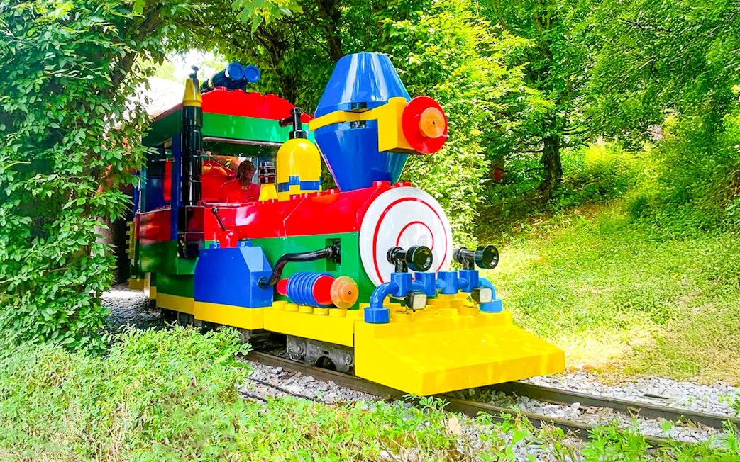 Colorful LEGO train ride at LEGOLAND Deutschland amidst greenery.