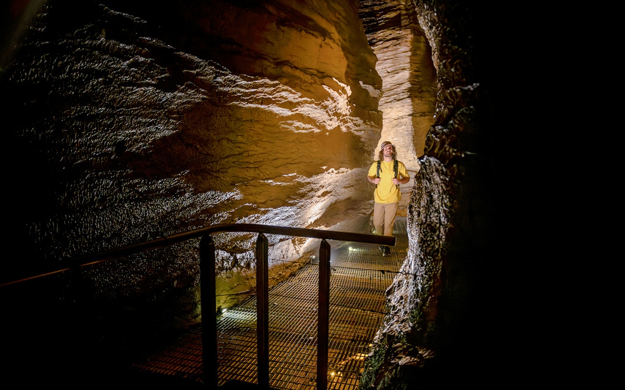 Tourist walking through illuminated Te Anau Glowworm Caves on guided tour.